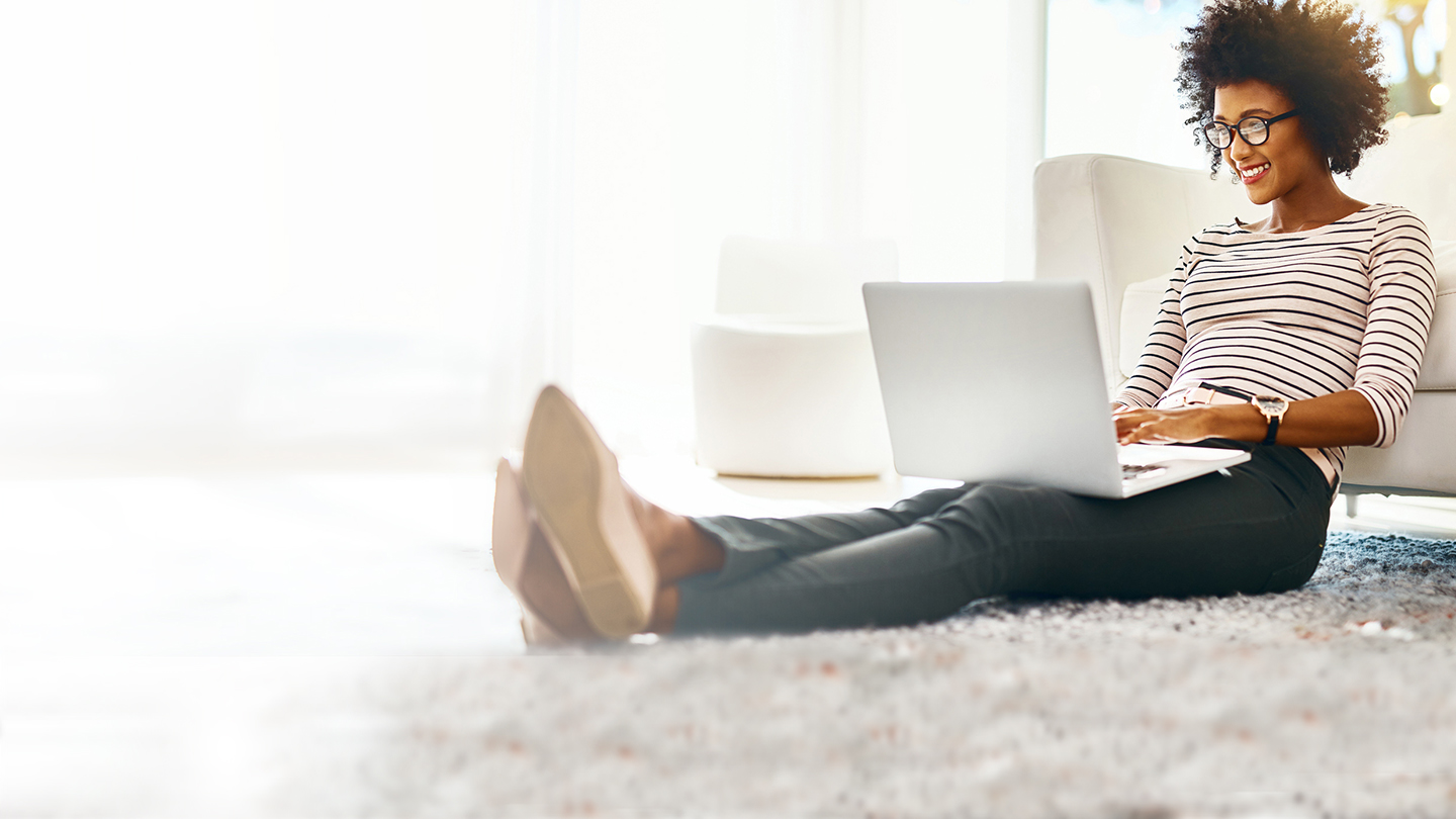 Shot of a cheerful young woman doing online shopping on her laptop while being seated on the floor at home